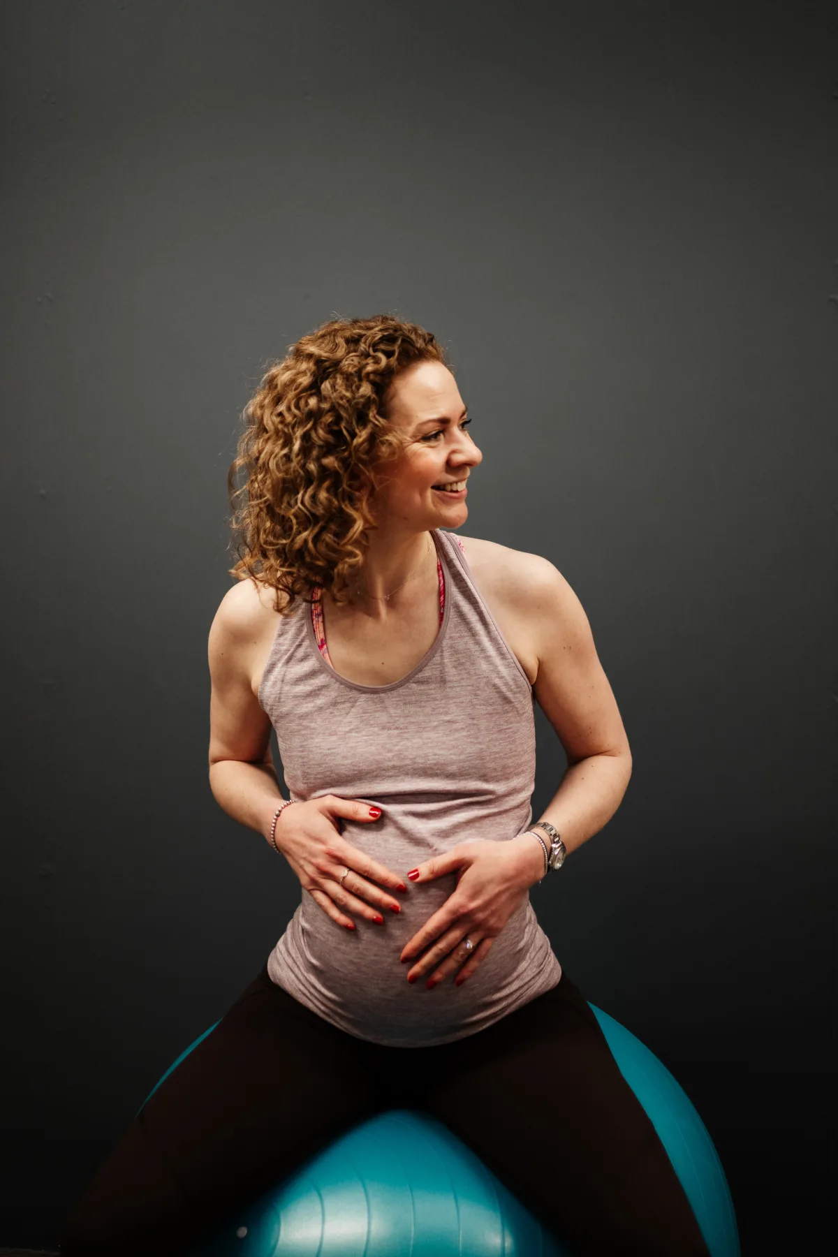 A mum-to-be seated on a birthing ball with her hands on her bump